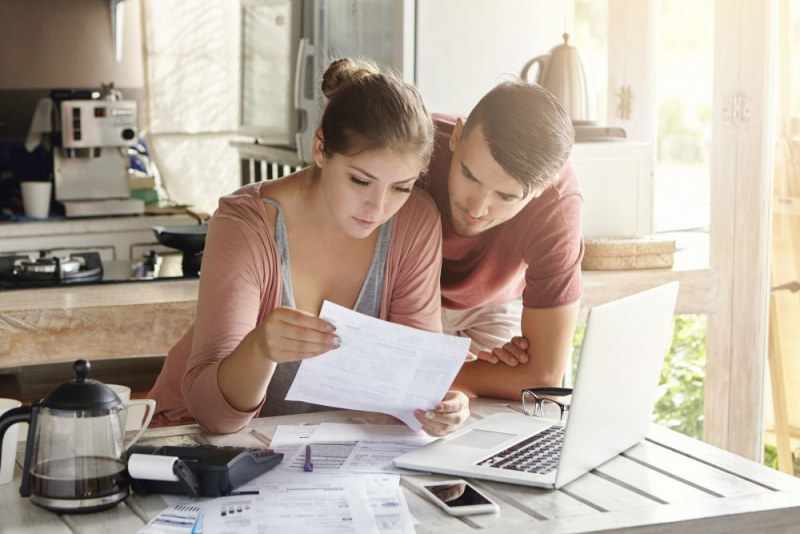 A man and woman reviewing financial documents in kitchen.